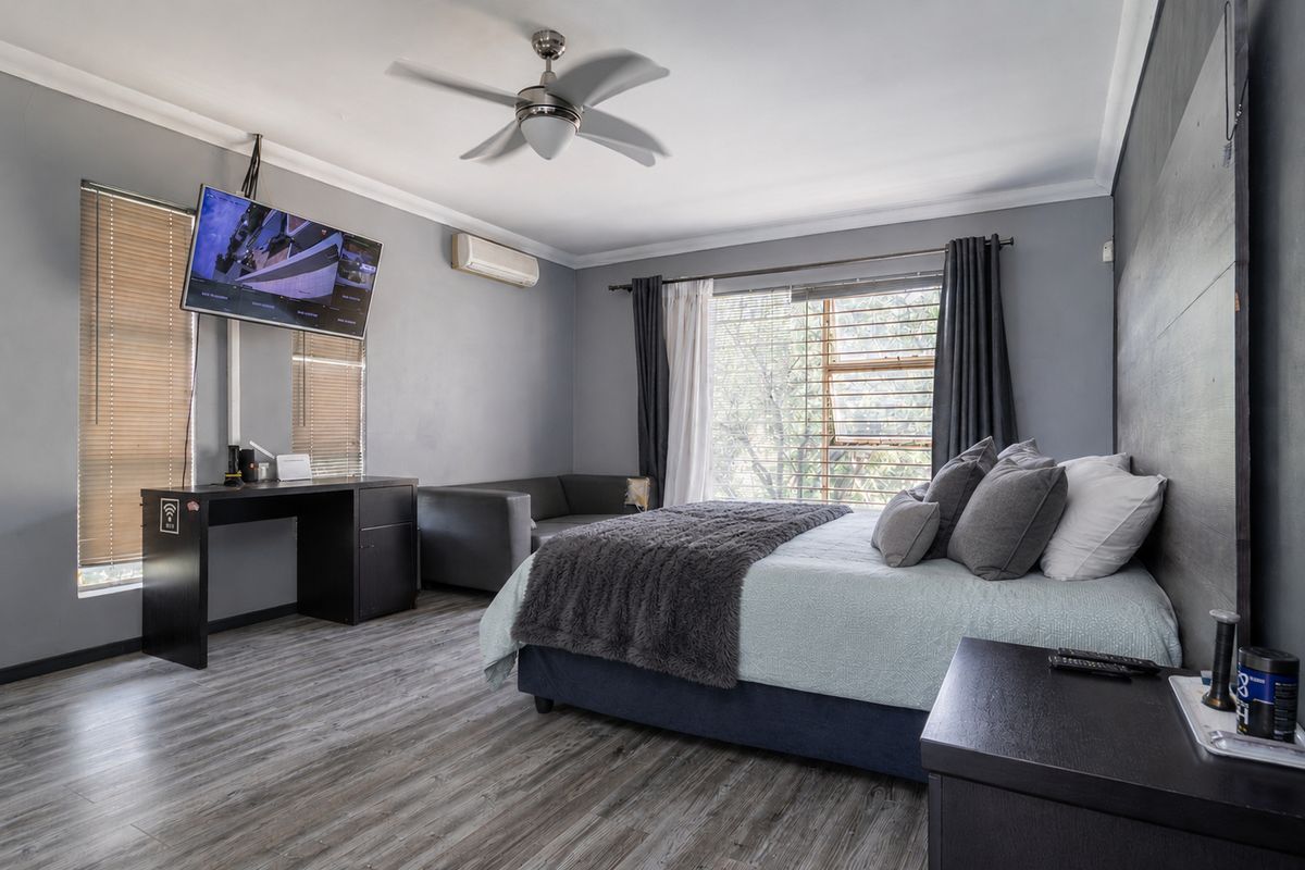 Spacious bedroom featuring laminate flooring, a ceiling fan, split-system air conditioning, and a modern feature wall panel.