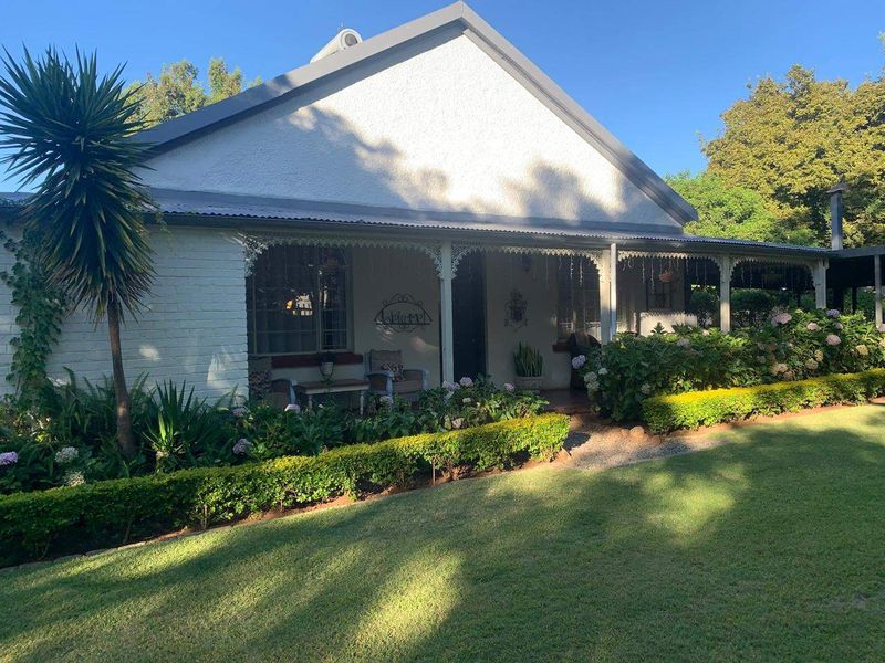 Charming cottage-style home featuring a covered veranda with decorative ironwork, set within a well-maintained garden with established landscaping.