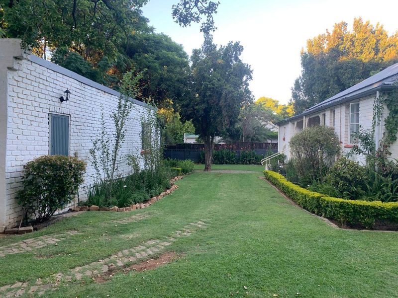 A well-maintained garden area situated between two brick structures, featuring a central lawn, established garden beds, and perimeter boundary walls.
