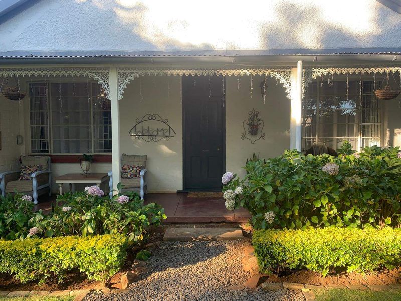Charming front facade featuring a covered veranda with decorative wrought iron fretwork, established garden beds, and a classic timber entrance door.