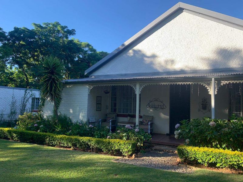Charming front facade featuring a covered veranda with decorative wrought iron fretwork, overlooking a well-maintained garden with manicured hedging.