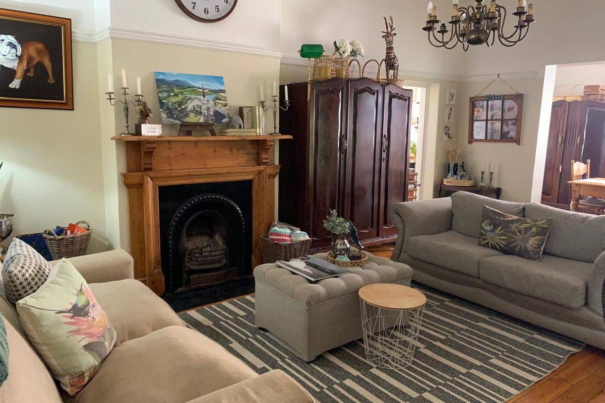 A traditional living room featuring a classic timber fireplace mantel, cast iron insert, and original timber flooring, complemented by decorative coving and a chandelier.