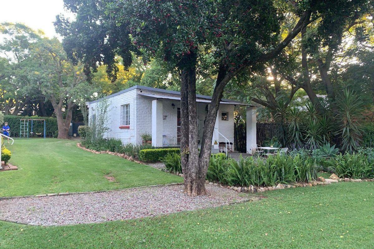A view of the rear exterior of the house featuring a painted brick facade, a covered patio area, and a well-maintained garden.