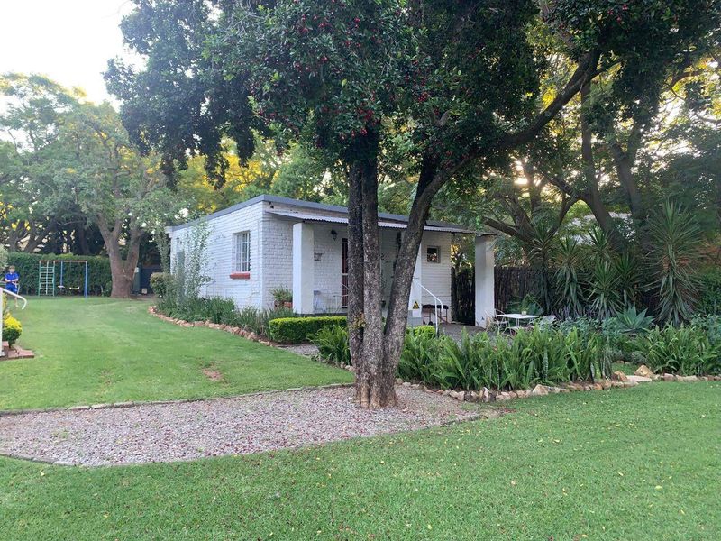A view of the rear exterior of the house featuring a painted brick facade, a covered patio area, and a well-maintained garden.
