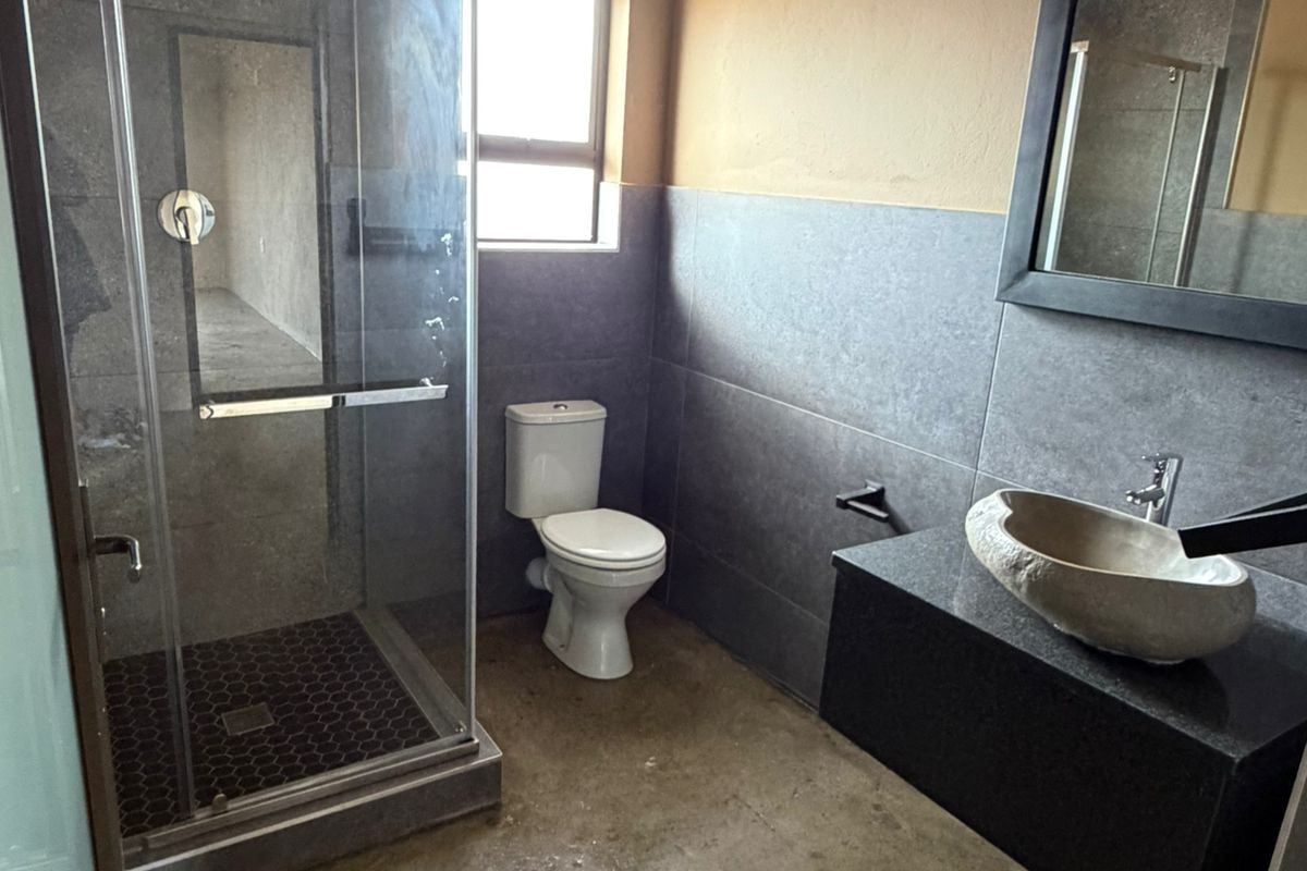 Modern bathroom featuring a glass shower enclosure, vessel sink on a floating vanity, and polished concrete flooring with neutral wall finishes.