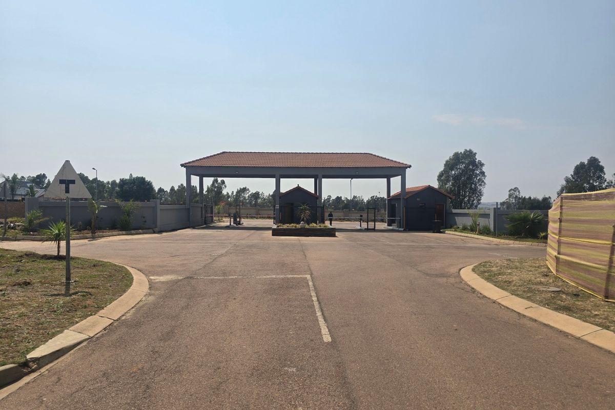 A view of the secure gated entrance to the residential estate, featuring a paved driveway and a covered security gatehouse.