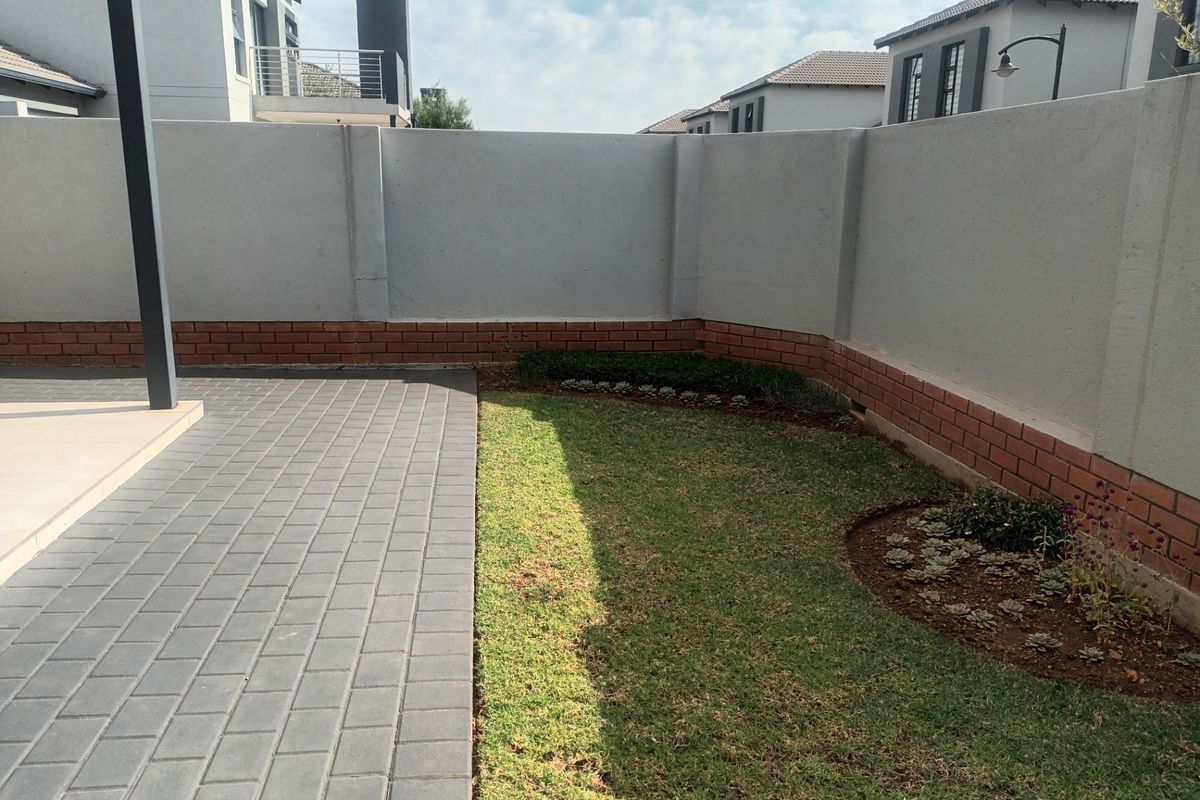 A private rear garden featuring a paved patio area, a well-maintained lawn, and a secure perimeter boundary wall with a brick base.