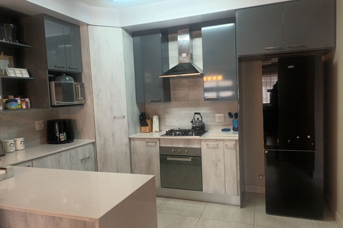 Modern kitchen featuring sleek grey and wood-grain cabinetry, stone countertops, integrated appliances, and a gas hob with an overhead extractor fan.
