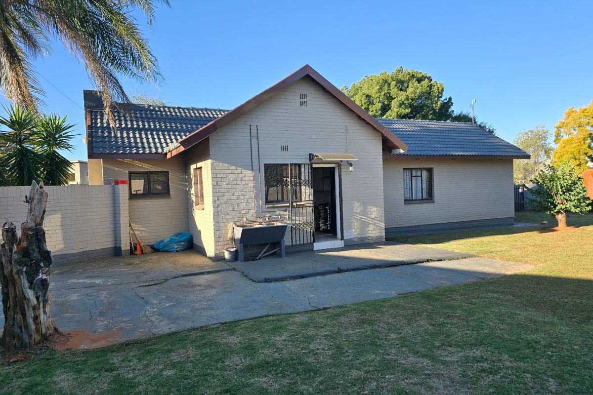 Rear view of a single-story brick house featuring a concrete patio, external wash basin, and security features on windows and doors.