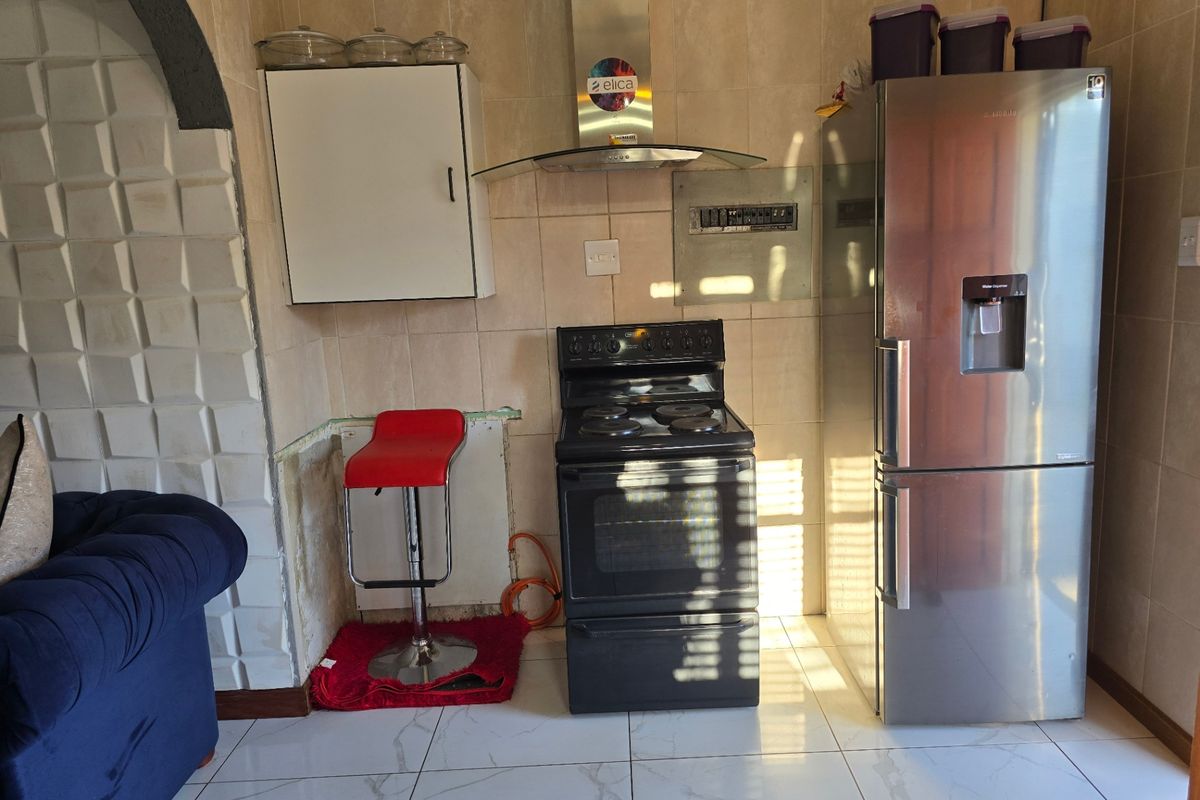 Kitchen area featuring tiled walls and flooring, an extractor fan, and a freestanding stove, with an unfinished section requiring cabinetry or countertop installation.