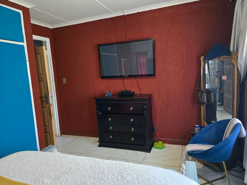 A bedroom featuring tiled flooring and a built-in cupboard, currently finished with textured red walls and requiring minor cosmetic updates.