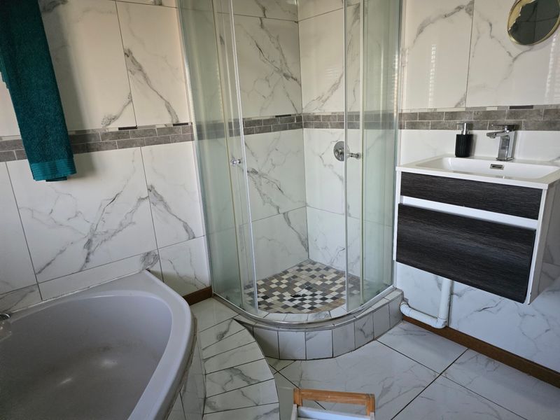 Modern bathroom featuring a corner shower enclosure, built-in bathtub, and a contemporary wall-mounted vanity unit with marble-effect wall tiles.