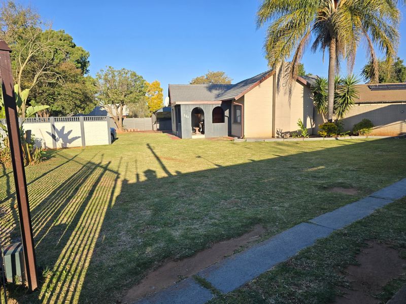 Front view of a single-story house featuring a tiled roof, arched entrance, and a spacious front lawn with perimeter walling.
