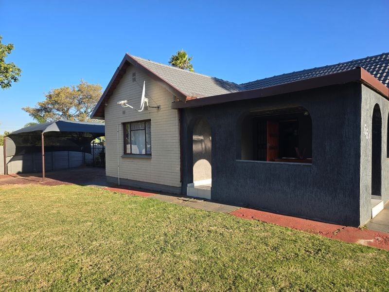 Front view of a single-story house featuring a tiled roof, brick and textured facade, covered patio area, and an adjacent carport.