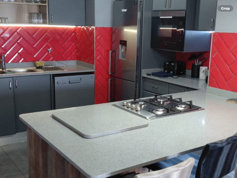 Modern kitchen featuring a central island with a gas hob, stone countertops, striking red herringbone tile backsplash, and integrated appliances.