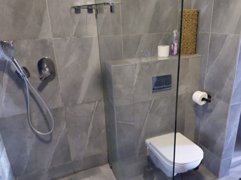 Modern bathroom featuring grey stone-look wall and floor tiles, a wall-mounted toilet with concealed cistern, and a glass shower screen.