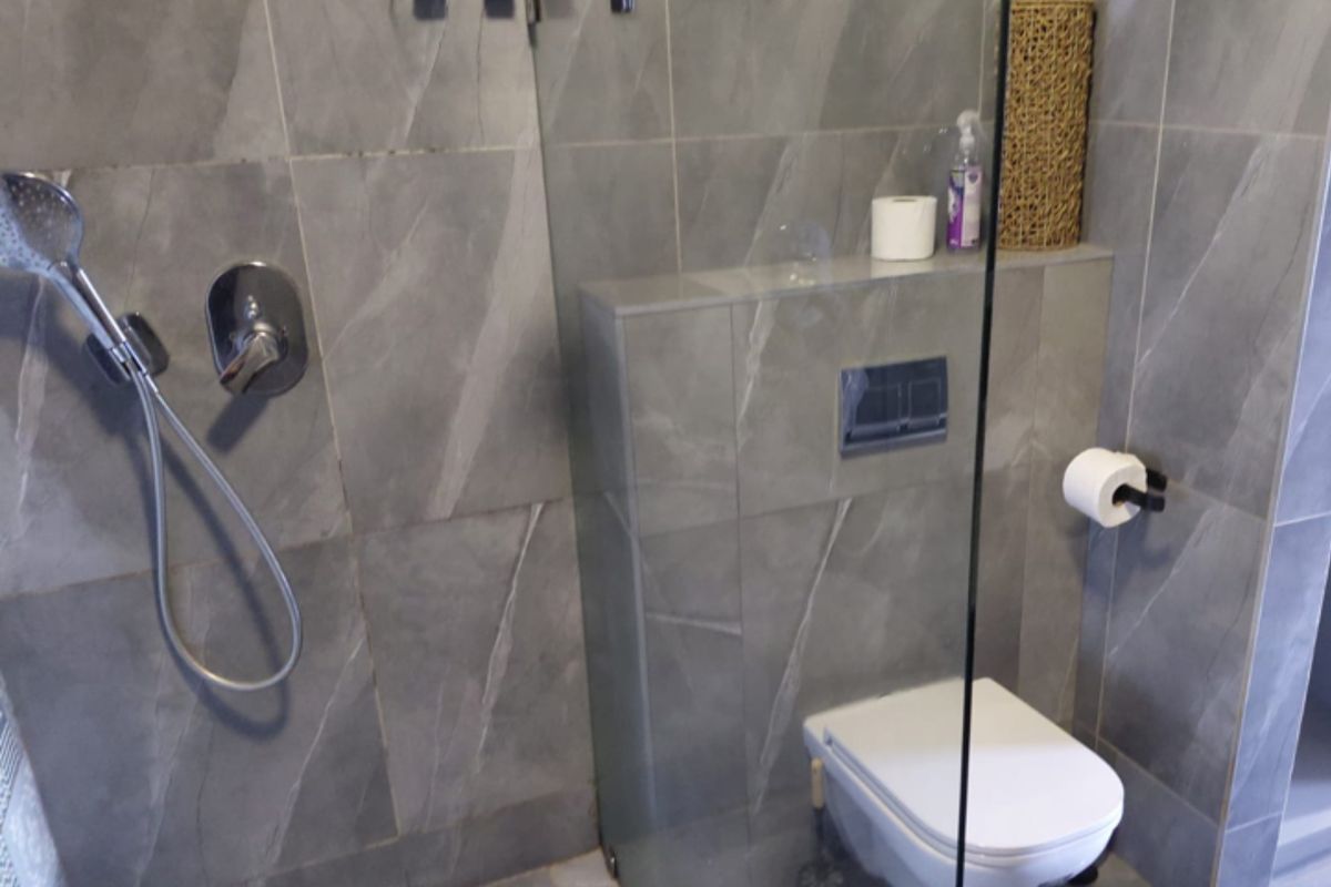 Modern bathroom featuring grey stone-look wall and floor tiles, a wall-mounted toilet with concealed cistern, and a glass shower screen.