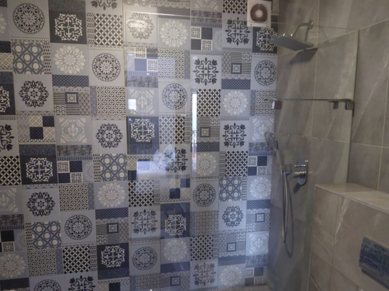 Modern bathroom shower area featuring decorative patterned wall tiles, a glass screen, and a dual-head shower system with built-in shelving.