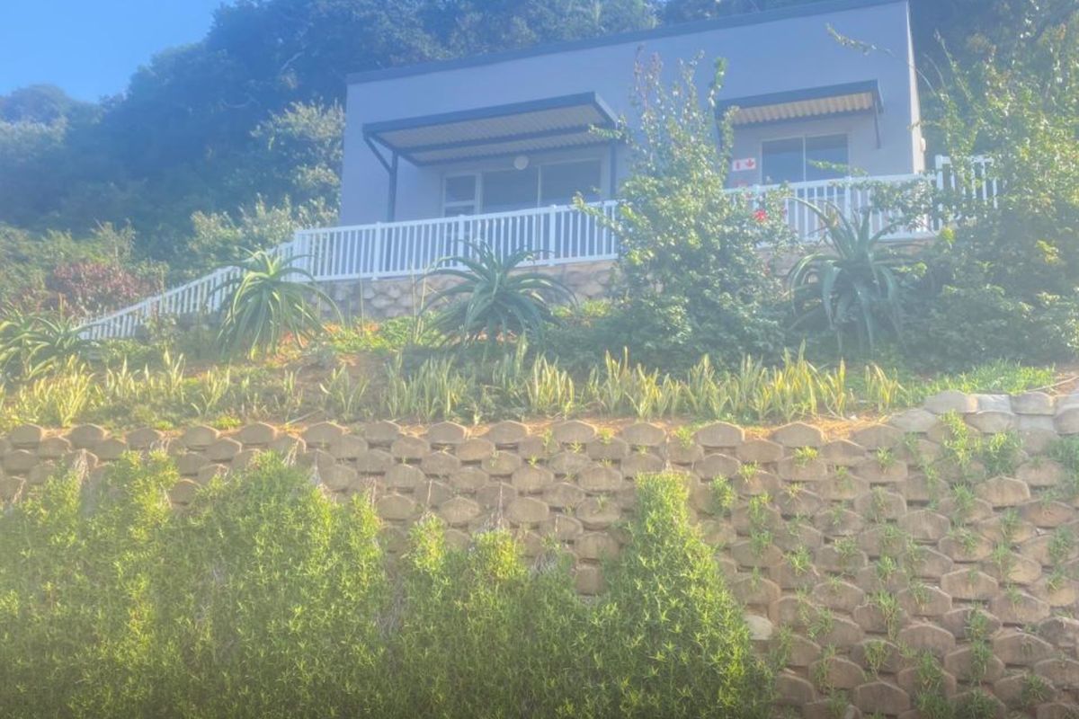 Rear view of the apartment featuring a terraced retaining wall, landscaped garden, and a balcony with white railing and overhead awning.
