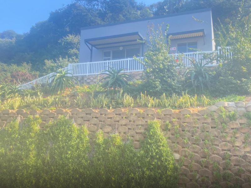 Rear view of the apartment featuring a terraced retaining wall, landscaped garden, and a balcony with white railing and overhead awning.