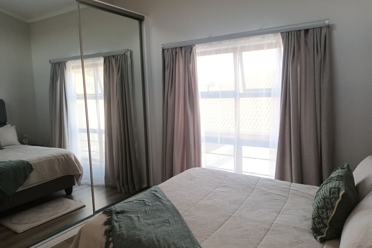 A well-maintained bedroom featuring laminate flooring and a large floor-to-ceiling mirrored sliding wardrobe, providing ample storage and reflecting natural light.