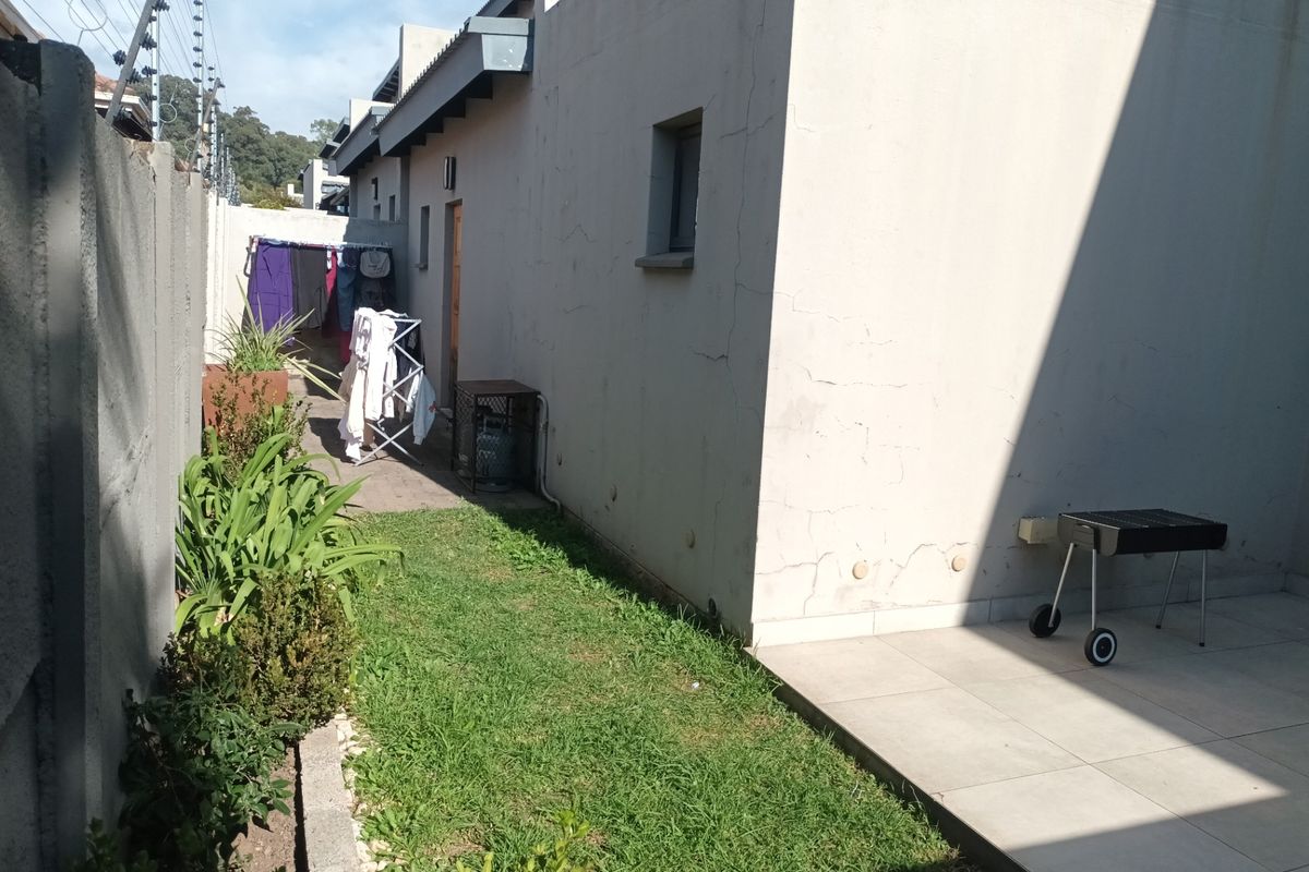 Rear exterior view of the townhouse featuring a small lawn, tiled patio area, and boundary wall with electric fencing.
