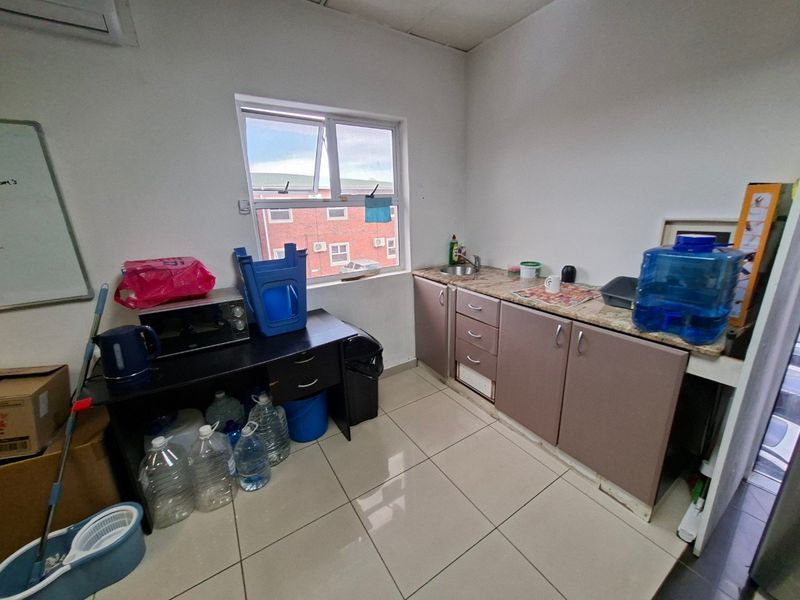 A functional scullery or kitchenette area featuring built-in cabinetry, a stainless steel sink, tiled flooring, and a window providing natural light.