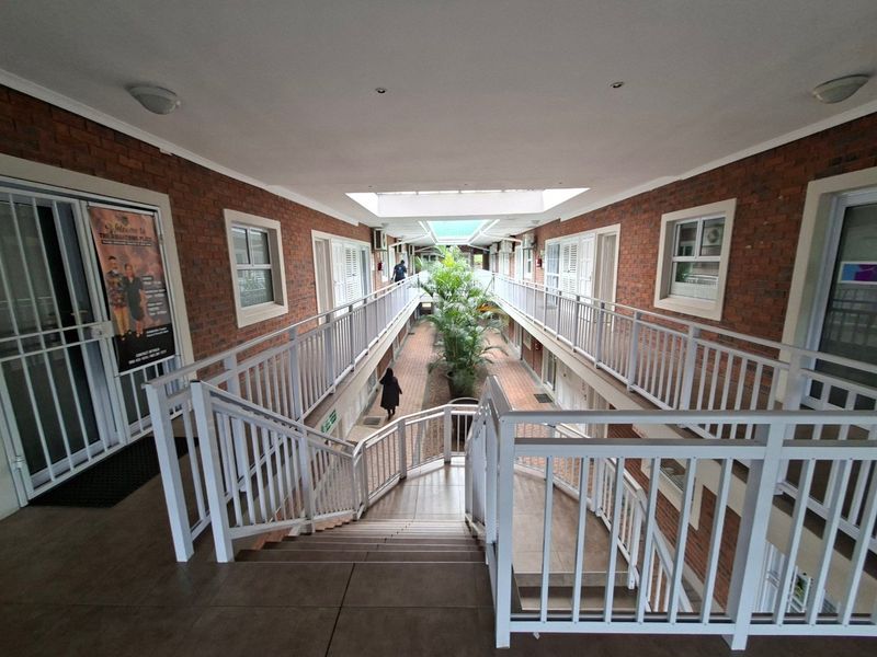 Open-air commercial corridor featuring exposed brick walls, a central skylight, and a paved courtyard area accessible via a tiled staircase.