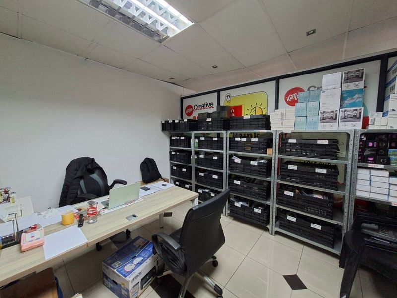 A functional commercial office space featuring tiled flooring, suspended ceiling lighting, and extensive metal shelving units for storage.