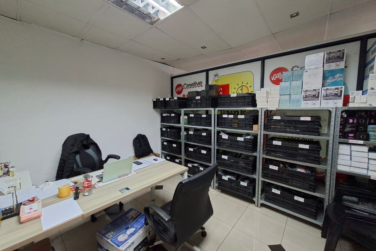 A functional commercial office space featuring tiled flooring, suspended ceiling lighting, and extensive metal shelving units for storage.