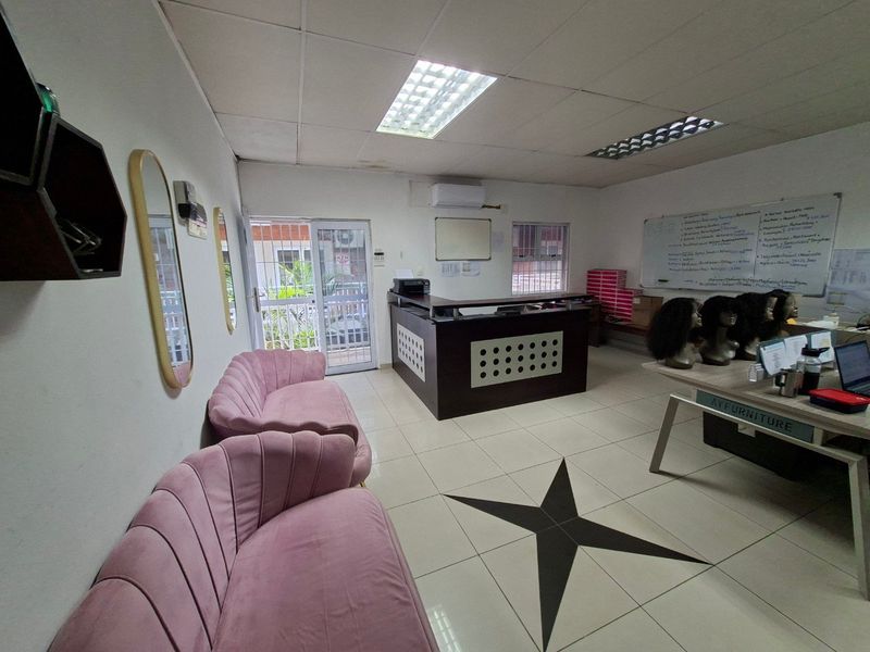 Commercial office space featuring a reception desk, tiled flooring, drop ceiling with integrated lighting, and a wall-mounted air conditioning unit.