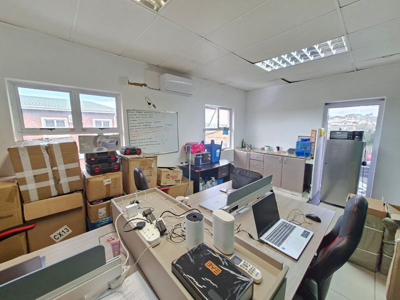 Commercial office space featuring a kitchenette, suspended ceiling, and split-system air conditioning, currently utilized for storage and workspace.