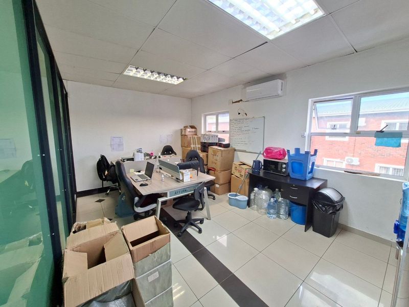 A functional commercial office space featuring tiled flooring, suspended ceiling with integrated lighting, and a wall-mounted air conditioning unit.