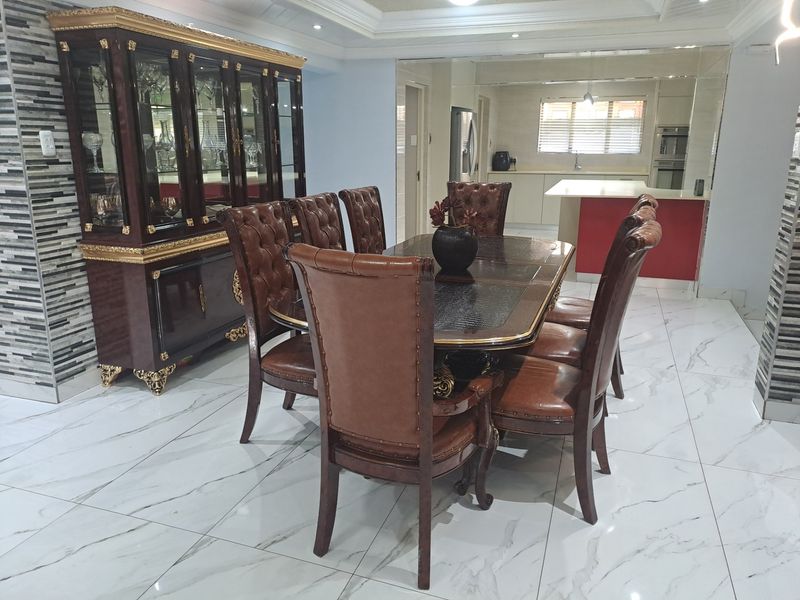 Spacious open-plan dining area featuring polished marble-look flooring, decorative stone wall cladding, and a seamless transition into a modern kitchen with built-in cabinetry.