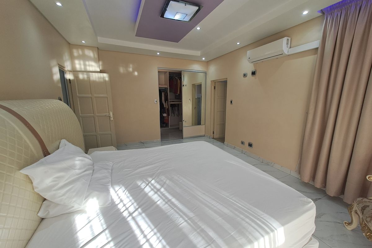 Spacious bedroom featuring a recessed ceiling with ambient lighting, tiled floors, a split-system air conditioner, and a convenient walk-in closet with mirrored doors.