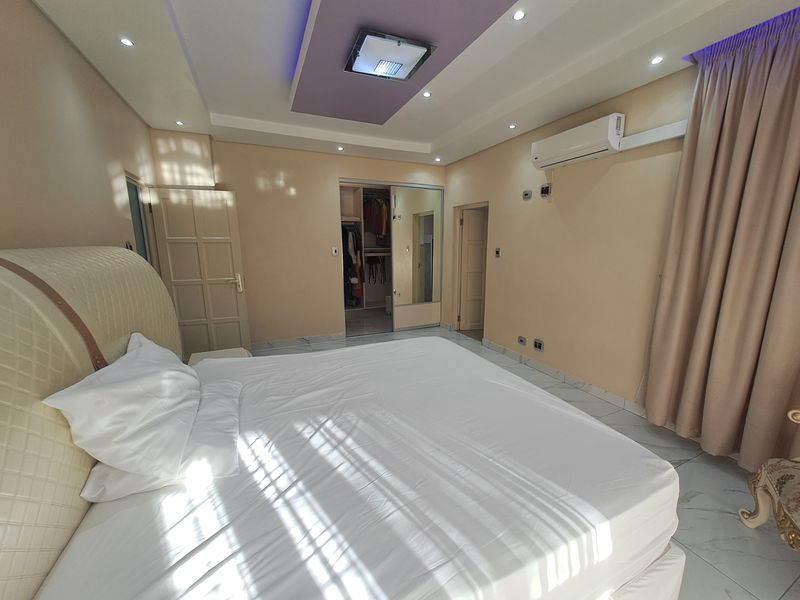 Spacious bedroom featuring a recessed ceiling with ambient lighting, tiled floors, a split-system air conditioner, and a convenient walk-in closet with mirrored doors.