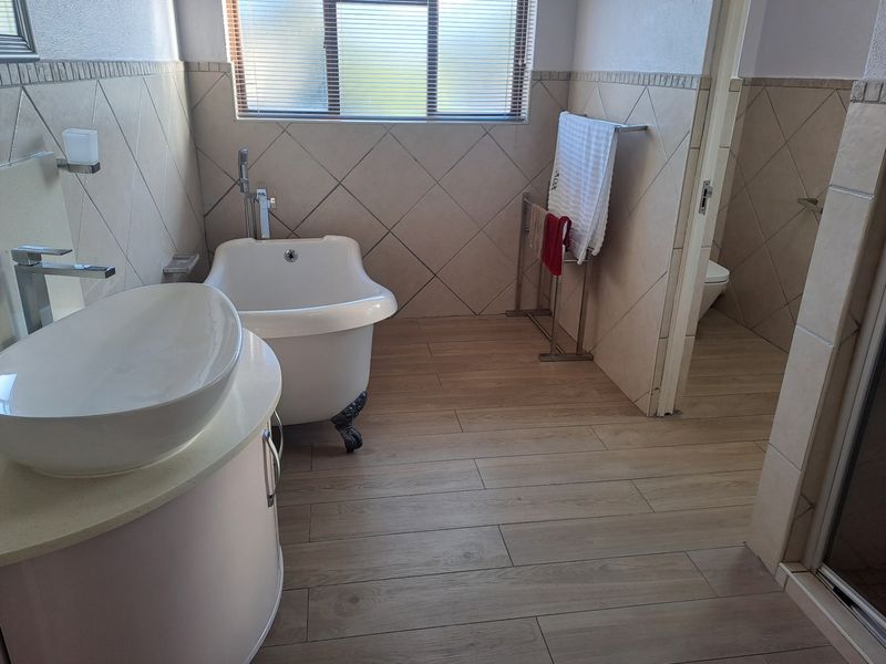 A well-maintained bathroom featuring a freestanding bathtub, modern vessel sink vanity, and neutral wood-look floor tiles with diamond-patterned wall tiling.
