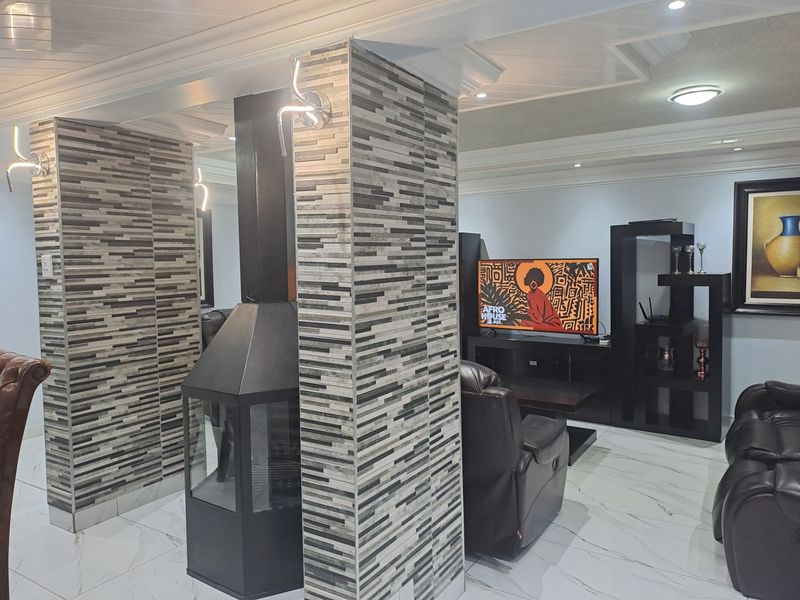 Spacious living area featuring a modern freestanding fireplace, decorative tiled columns, recessed ceiling lighting, and polished marble-look floor tiles.