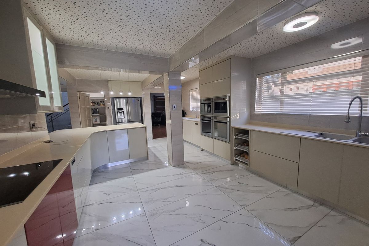 Modern, spacious kitchen featuring high-gloss cabinetry, stone countertops, integrated appliances, and marble-look floor tiles with ample workspace and recessed lighting.