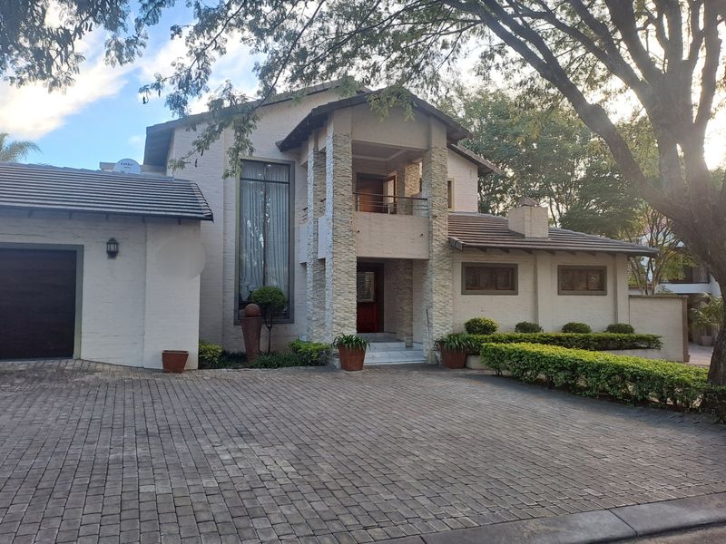 A well-maintained double-story residence featuring stone cladding, a paved driveway, a tiled roof, and a covered entrance with an upper-level balcony.