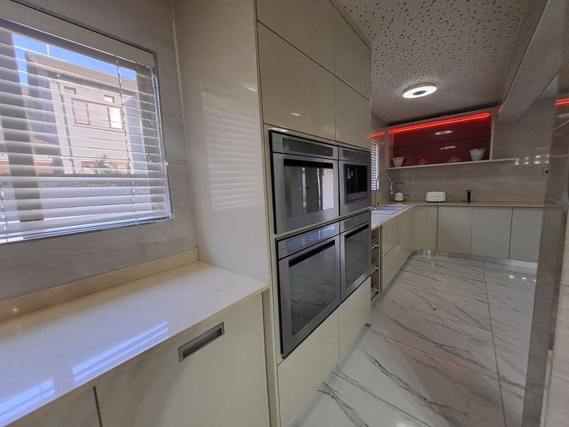 Modern kitchen featuring high-gloss cabinetry, integrated double ovens, stone countertops, marble-look flooring, and stylish LED accent lighting.