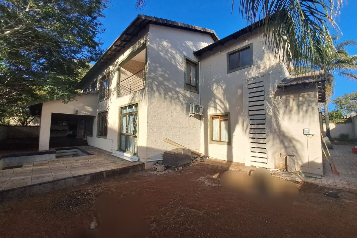 Rear view of a two-story house featuring a tiled patio, balcony, and an unlandscaped garden area.
