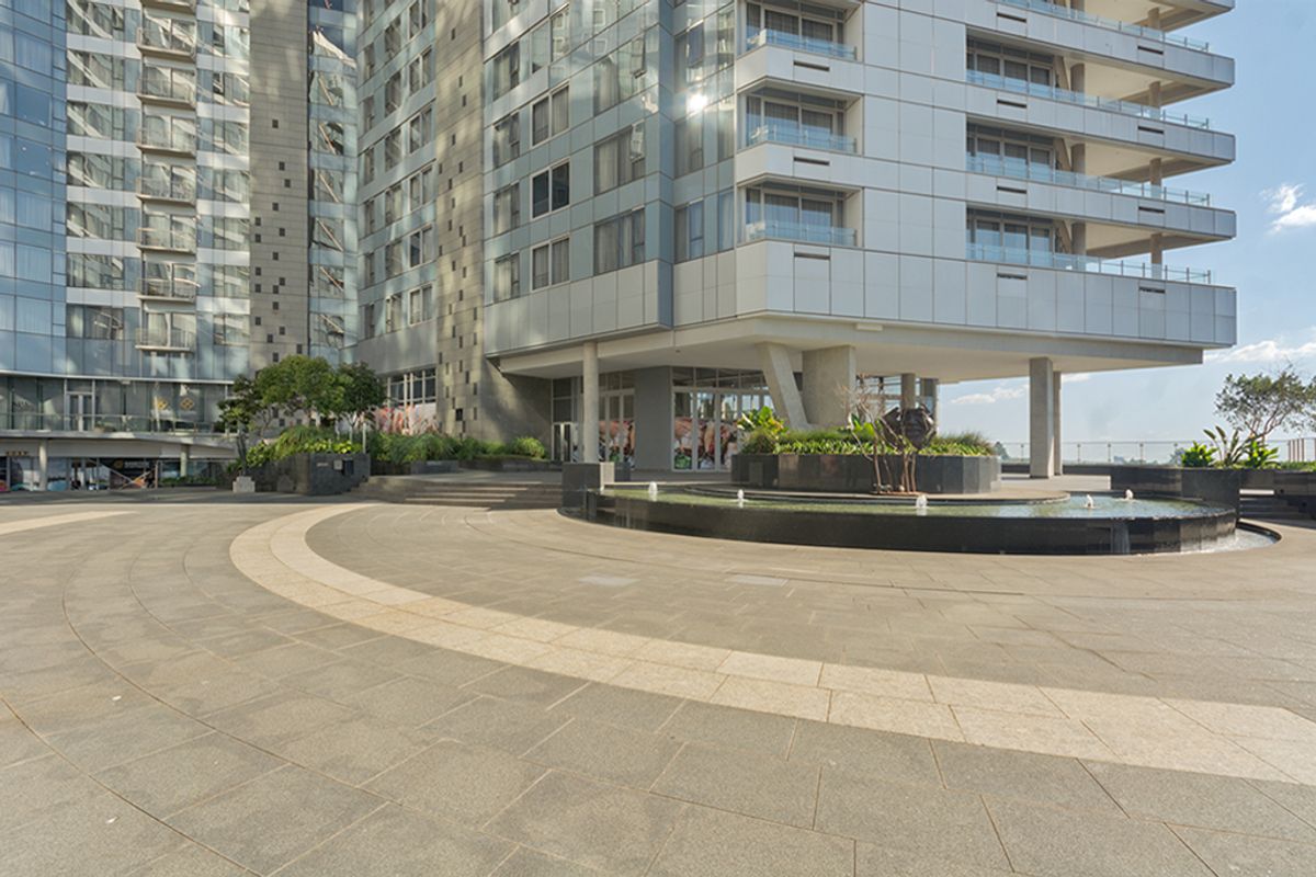 Modern commercial building exterior featuring a large stone-paved plaza, integrated water feature, and contemporary glass and metal facade.