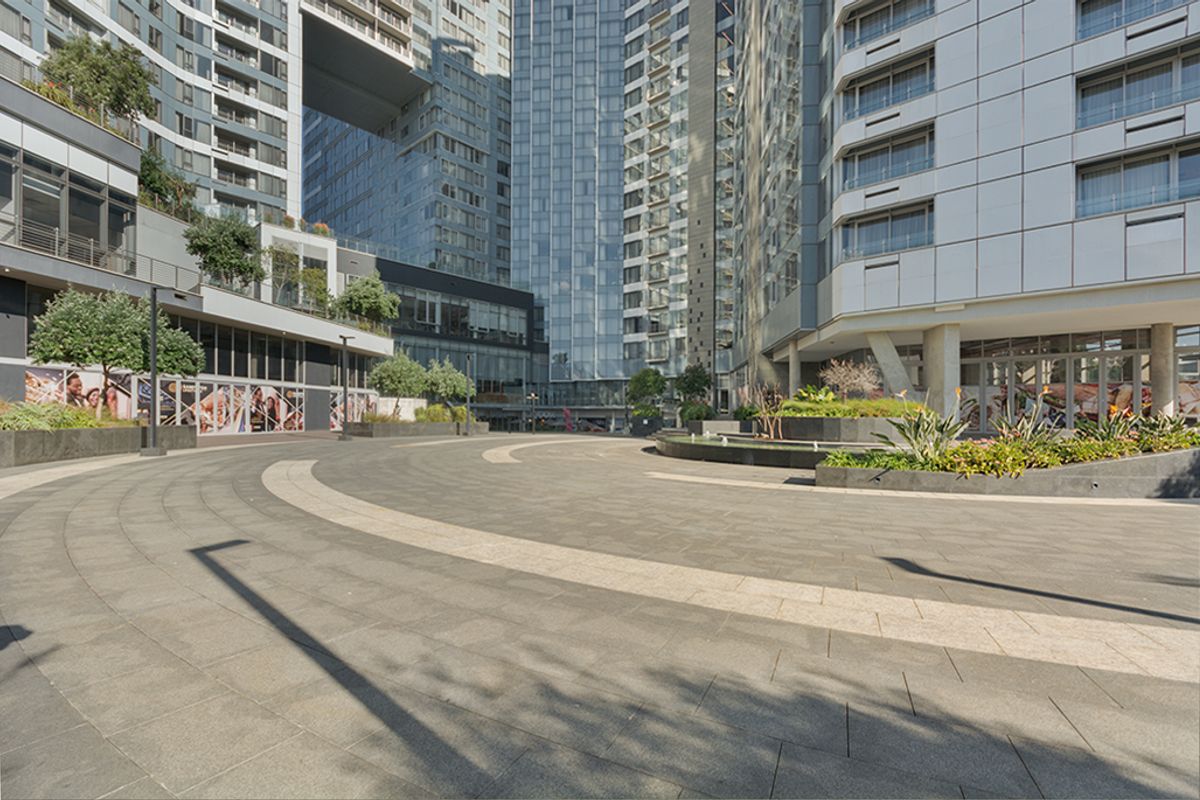 A modern commercial courtyard featuring paved walkways, landscaped planters, and a water feature surrounded by contemporary high-rise glass buildings.