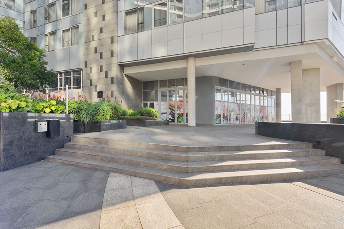 Modern commercial building entrance featuring stone-tiled stairs, granite cladding, and a prominent glass facade with integrated landscaping.
