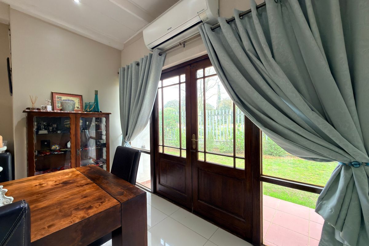 A bright living area featuring tiled flooring, a wall-mounted air conditioning unit, and timber-framed glass double doors providing direct access to the garden.