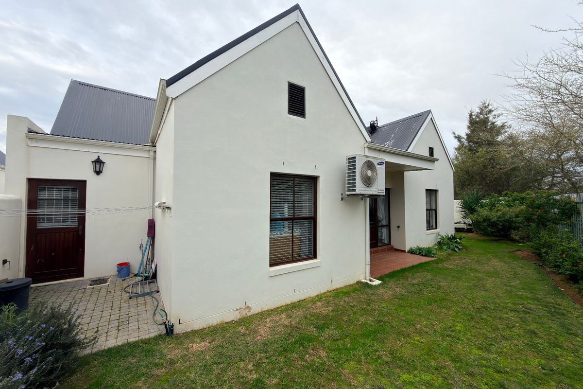 Rear view of the property featuring a paved patio area, established garden, and exterior wall-mounted air conditioning unit.