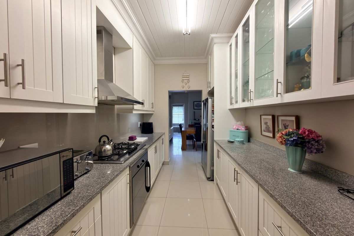 A well-maintained galley kitchen featuring white shaker-style cabinetry, granite countertops, a gas hob with extractor fan, and elegant glass-fronted display cabinets.