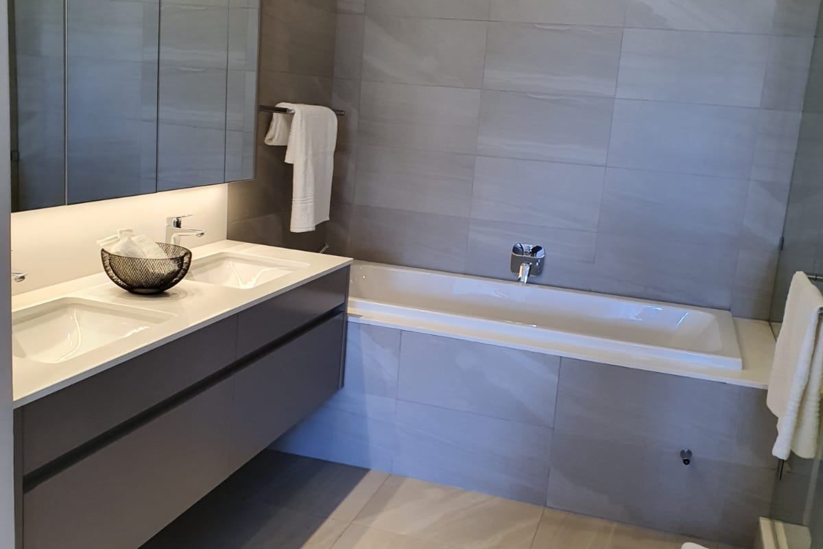 Modern bathroom featuring a double vanity with mirrored cabinetry, a built-in bathtub, and neutral floor-to-ceiling tiling.