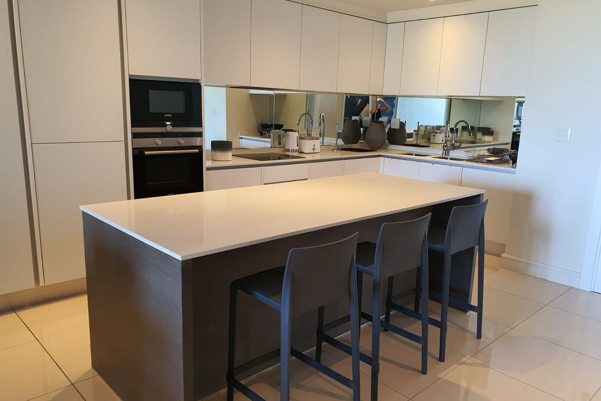 Modern kitchen featuring sleek white cabinetry, a central island with stone countertop, integrated appliances, and a mirrored splashback.